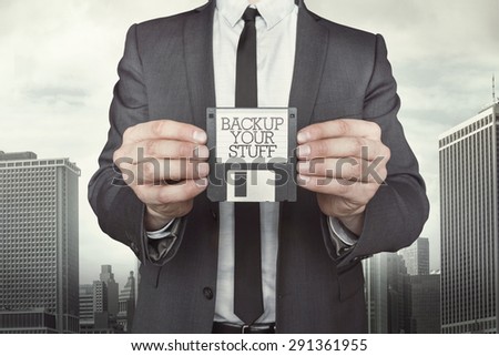 Businessman holding diskette in hands which reads backup your stuff on cityscape background