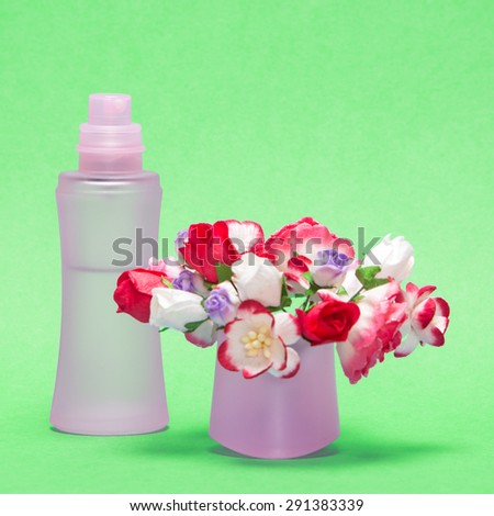 Floral perfume. Close-up of perfume bottle behind bouquet of flowers in its cap. Focus on bottle. Green background
