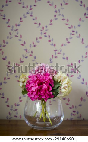 Artificial flowers arranged in a glass vase on a wooden surface.