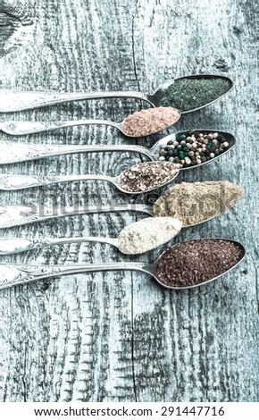 Antic metal spoons with different kinds of spices on old wooden board. Selective focus. Toned.