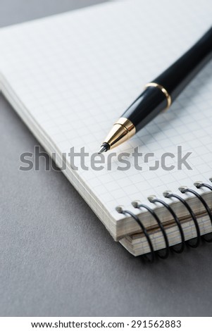 A spiral notebook with black ball pen on the grey table