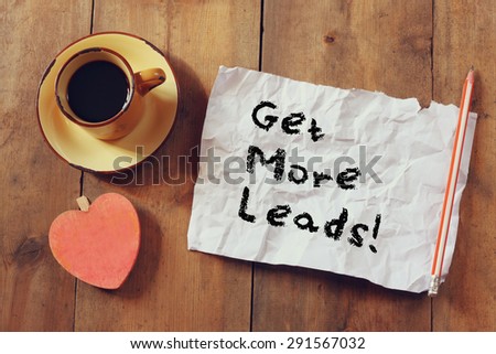 top view image of coffee cup, heart shape and paper with the phrase get more leads over wooden background