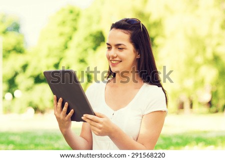 lifestyle, summer, vacation, technology and people concept - smiling young girl with tablet pc computer sitting on grass in park
