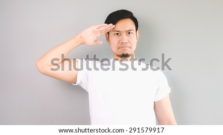 A man in salute pose and serious face. An asian man with white t-shirt and grey background. Royalty-Free Stock Photo #291579917