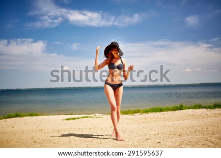 Pretty girl in bikini and hat spending summer vacation on beach