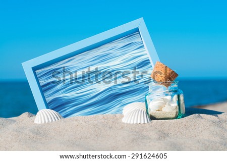 Blue picture frame, glass jar with cork lid and white shells on sandy beach; Holiday memories