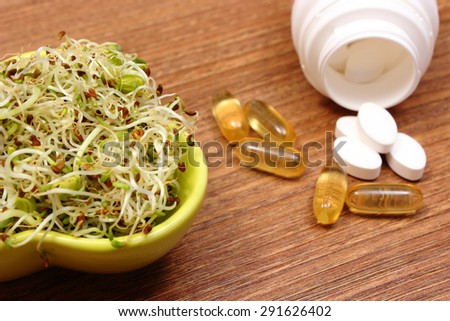 Bowl with alfalfa and radish sprouts and tablets supplements lying on wooden surface, choice between healthy eating and pills, healthy lifestyle food and nutrition