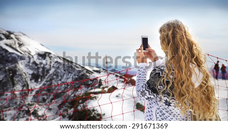 Blond woman photographing winter landscape mountains and snow with cell phone