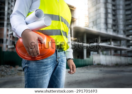 Closeup photo of engineer with hardhat and blueprints posing on building site