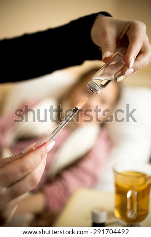 Closeup photo of woman filling syringe from ampule at sick girl's bed