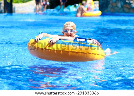 Happy kid, blonde caucasian boy, having fun floating and sliding in water park on inflatable ring enjoying sunny summer vacations in tropical resort