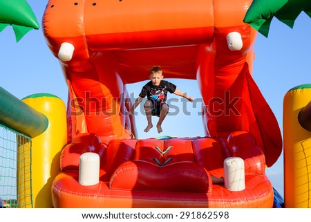 Small boy (6-8 years) wearing t-shirt and shorts jumping bare foot in the air on a colorful bouncy castle, blue sky in background