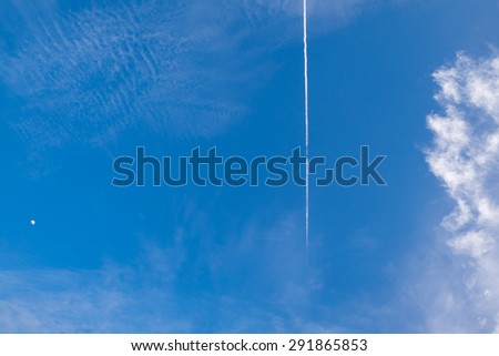 Airplane condensation trail or contrail with line of cloud over blue sky background and moon