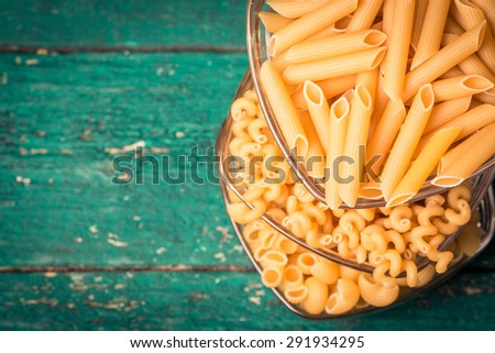 Various mix of pasta on wooden rustic background, sack,bowl, and wooden spoons. Diet and food concept.