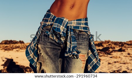 Tanned slim Model in the Desert in fashionable torn Jeans and checkered Shirt.