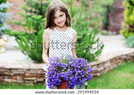 Adorable smiling kid girl in elegant dress holding flowers in the garden