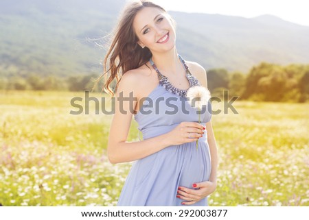 Happy pregnant woman, is wearing blue dress holding in hands dandelion flower outdoors, new life concept