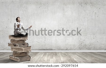Young businessman sitting on pile of old books and meditating