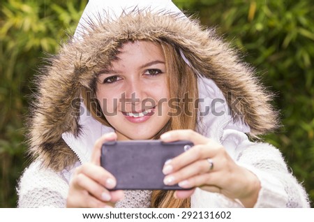 Model in outdoors environment holding her phone up towards camera as in taking a picture