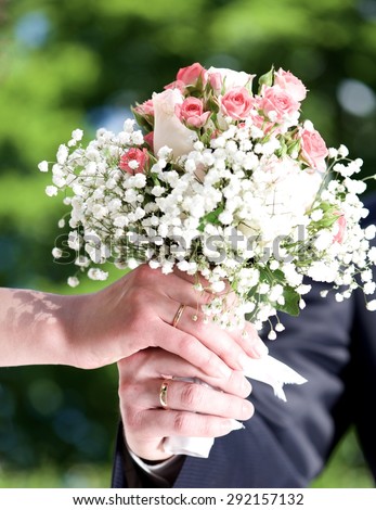 Two hands holding bouquet of roses on wedding day, two hands with the rings on wedding day in nice green booked background, conceptual photo of new family on wedding day