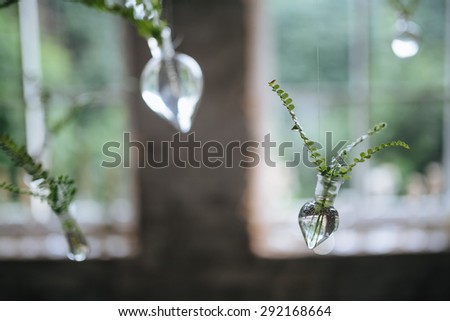 Composition of greens and glass bulbs hanging on a metal spring in the loft with a large window overlooking the garden
