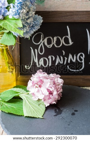 Blue and pink hydrangea in a vase with good morning note on the blackboard