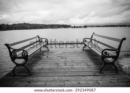 Black and white photo of the two benches with water and sky in the background.