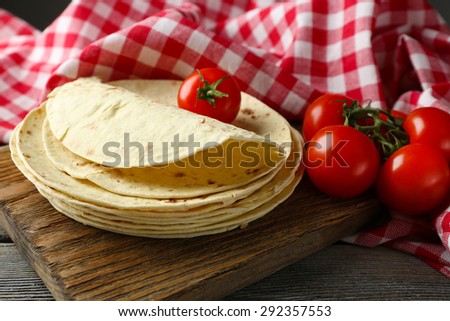 Stack of homemade whole wheat flour tortilla and vegetables on cutting board, on wooden table background