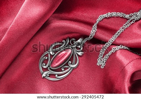 Silver vintage pendant on red silk as a background