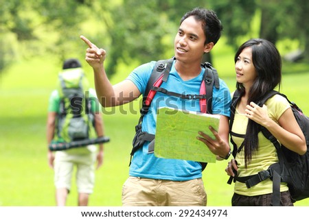 A portrait of a young asian couples backpacking looking at a map, outdoor