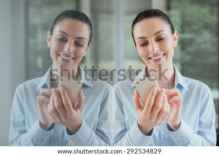 Beautiful smiling young woman using a smart phone, leaning on a window and reflecting on glass 