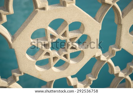 Islamic star pattern architectural detail on fence in front of bright blue water background