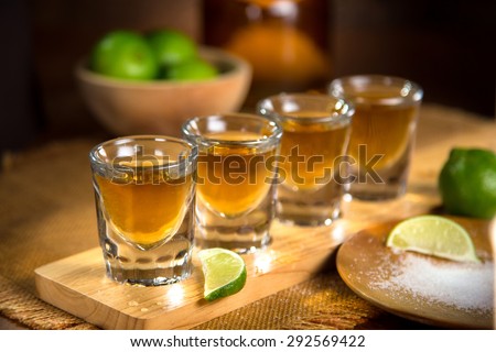 Four shot glasses with tequila bottle and bowl of limes with salt at a bar Royalty-Free Stock Photo #292569422