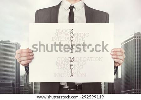 Social media crossword concept on paper what businessman is holding on cityscape background