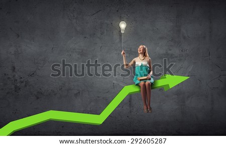 Young woman sitting on arrow with book in hands