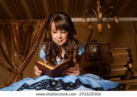 Little girl in a blue dress on the floor in room reading a book