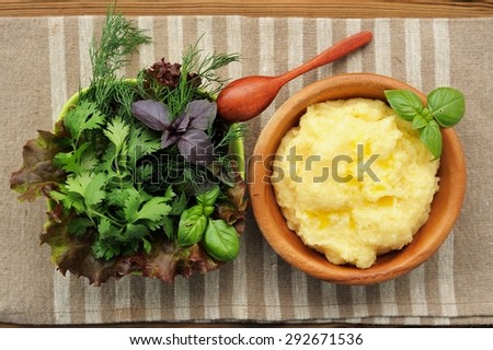Polenta with basil shoot in wooden bowl with green salad bowl and wooden spoon