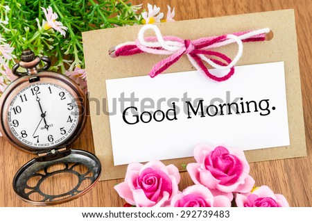 Good morning in greeting card and pocket watch on wooden background.