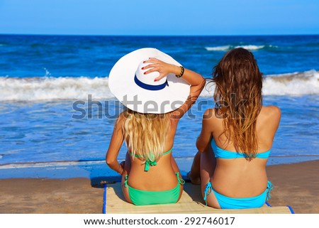 Beach girls rear back view sitting in the beach looking horizon in summer