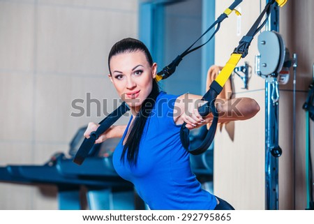 Young attractive woman training with htrx fitness straps in the gym's studio