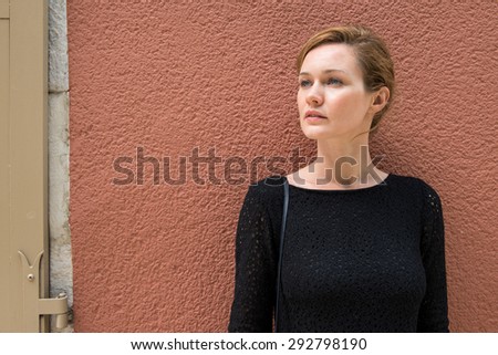 A woman is standing. In the background terracotta wall.