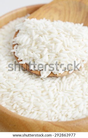 Raw rice in wooden bowl with spoon on white background.