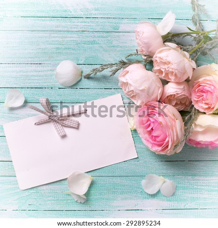 Postcard with fresh roses flowers and empty tag for your text on turquoise painted wooden background. Selective focus. Square image.
