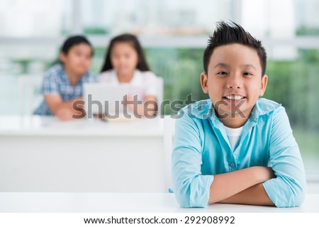 Asian preteen boy in the classroom, his classmates talking in the background Royalty-Free Stock Photo #292908992