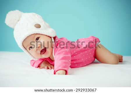 Little baby in knit winter clothing closing face with knitted beanie on the bed in the blue bedroom, New family and baby protection concept