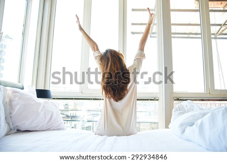 Woman stretching in bed after wake up, back view Royalty-Free Stock Photo #292934846