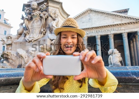 A laughing brunette tourist holds up her mobile phone and checking a photo she has taken. Behind her, Rome's Pantheon fountain and Pantheon.