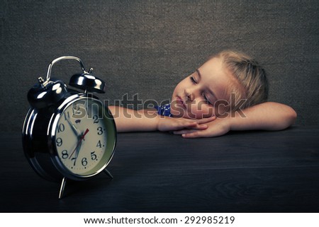 The sleeping little girl with a vintage alarm clock. It is stylized under a retro the photo