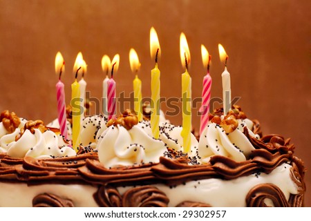 Birthday cake, lit candles on brown background
