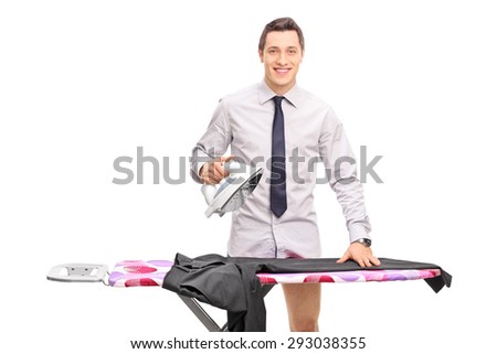 Young man with a gray shirt and tie ironing his pants on an ironing board and looking at the camera isolated on white background